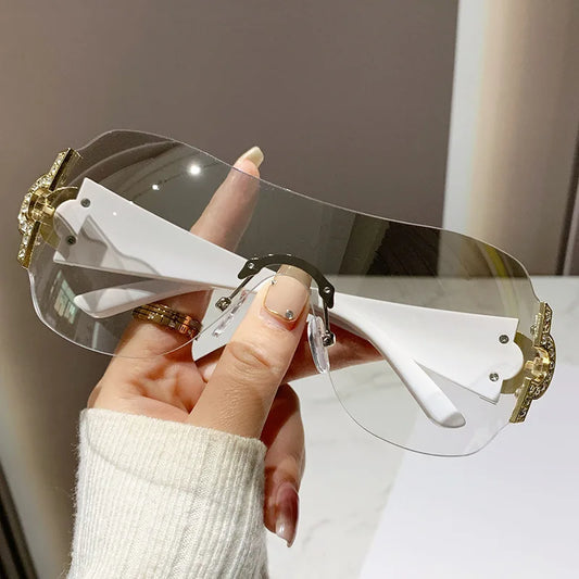 Sunglasses with gold and white frame held by a hand against a neutral background