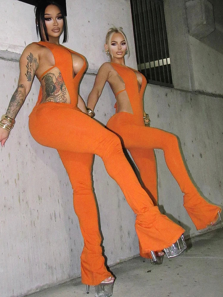 Two women in orange outfits posing against a concrete wall.