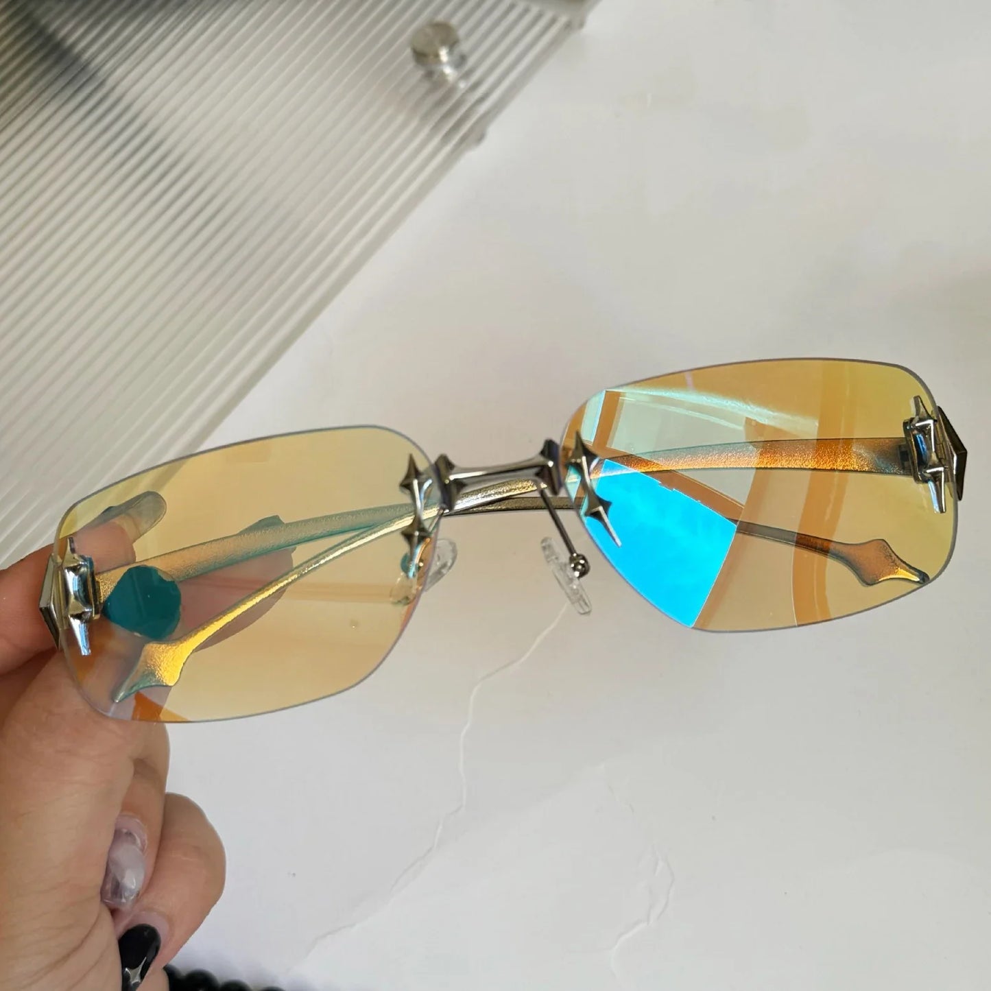 Gold-rimmed sunglasses with blue lenses held by a hand on a white background